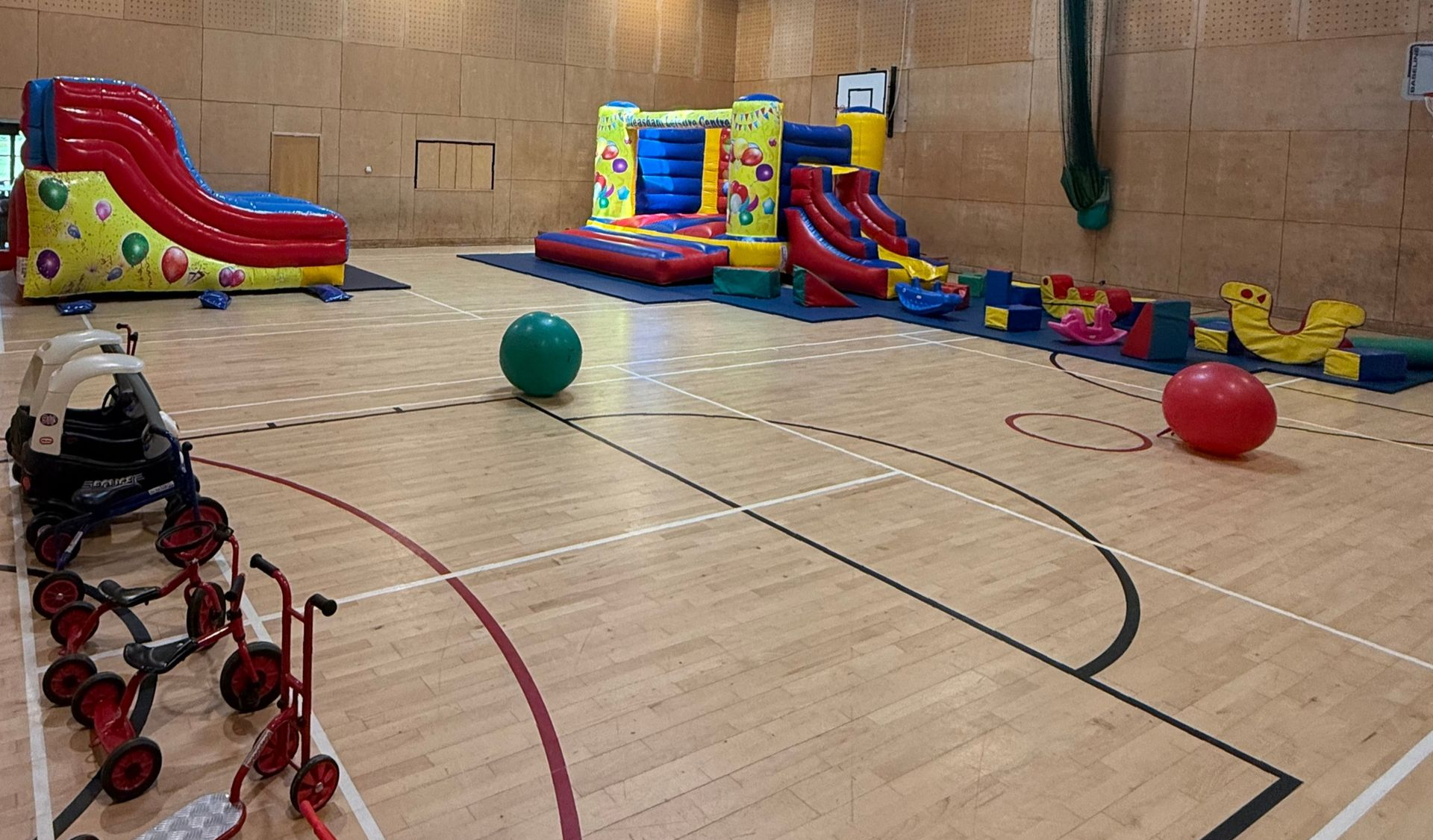 Indoor gym with colorful inflatable obstacle courses and exercise balls on a wooden court