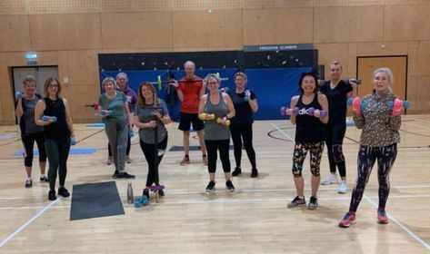 Group fitness class in a gym, people dancing and exercising on a hardwood floor.