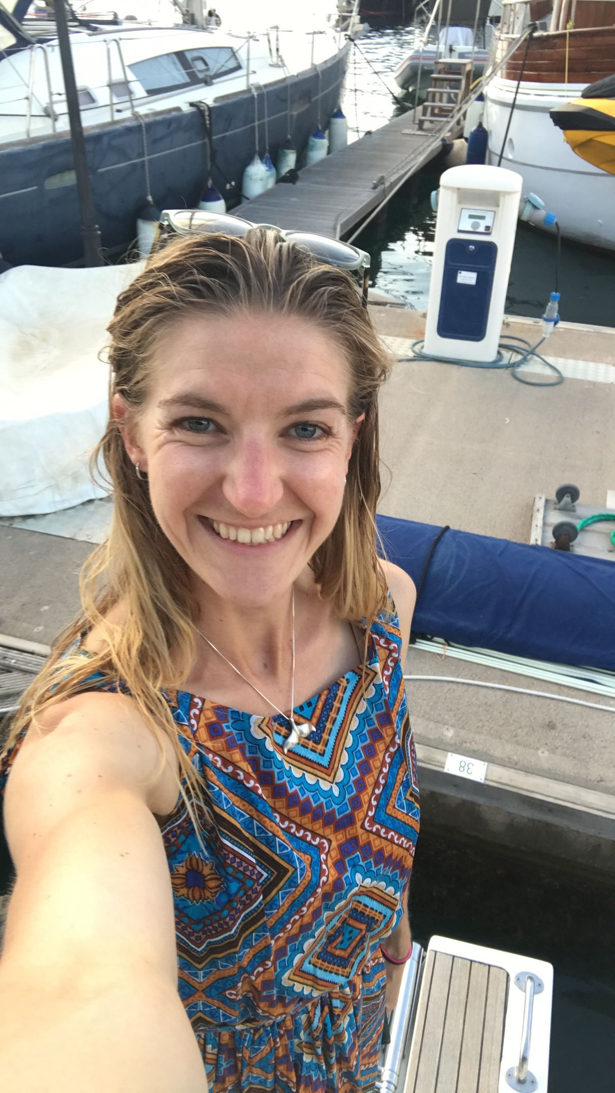 Smiling woman taking a selfie on a boat dock, with colorful boats and water in the background.