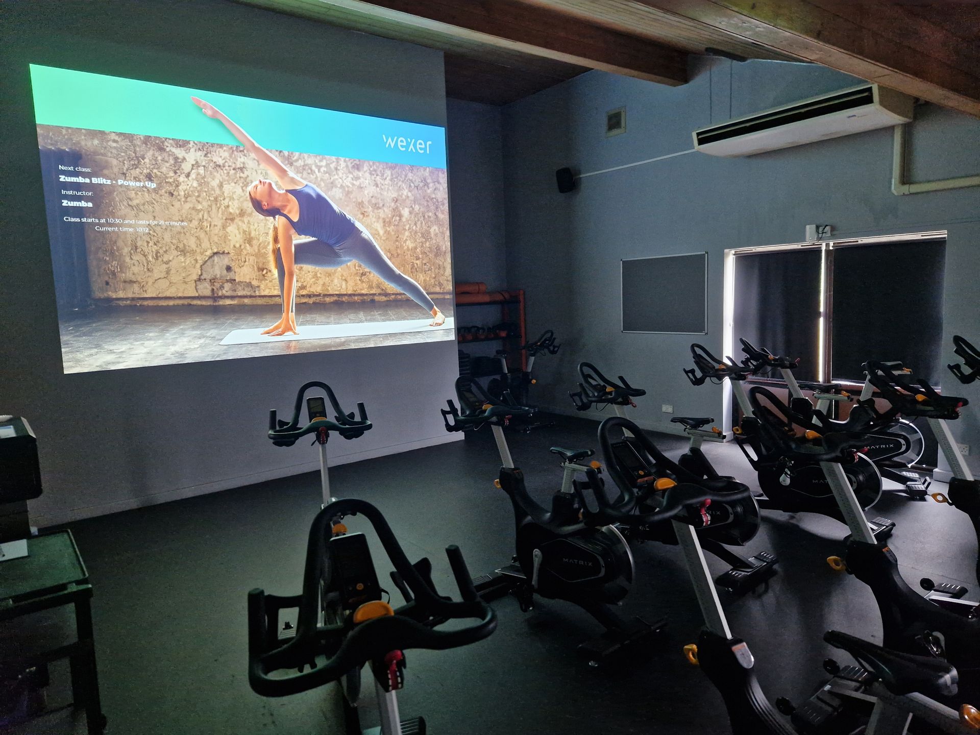 Indoor gym with stationary bikes facing a wall projection of a yoga pose on a beach.