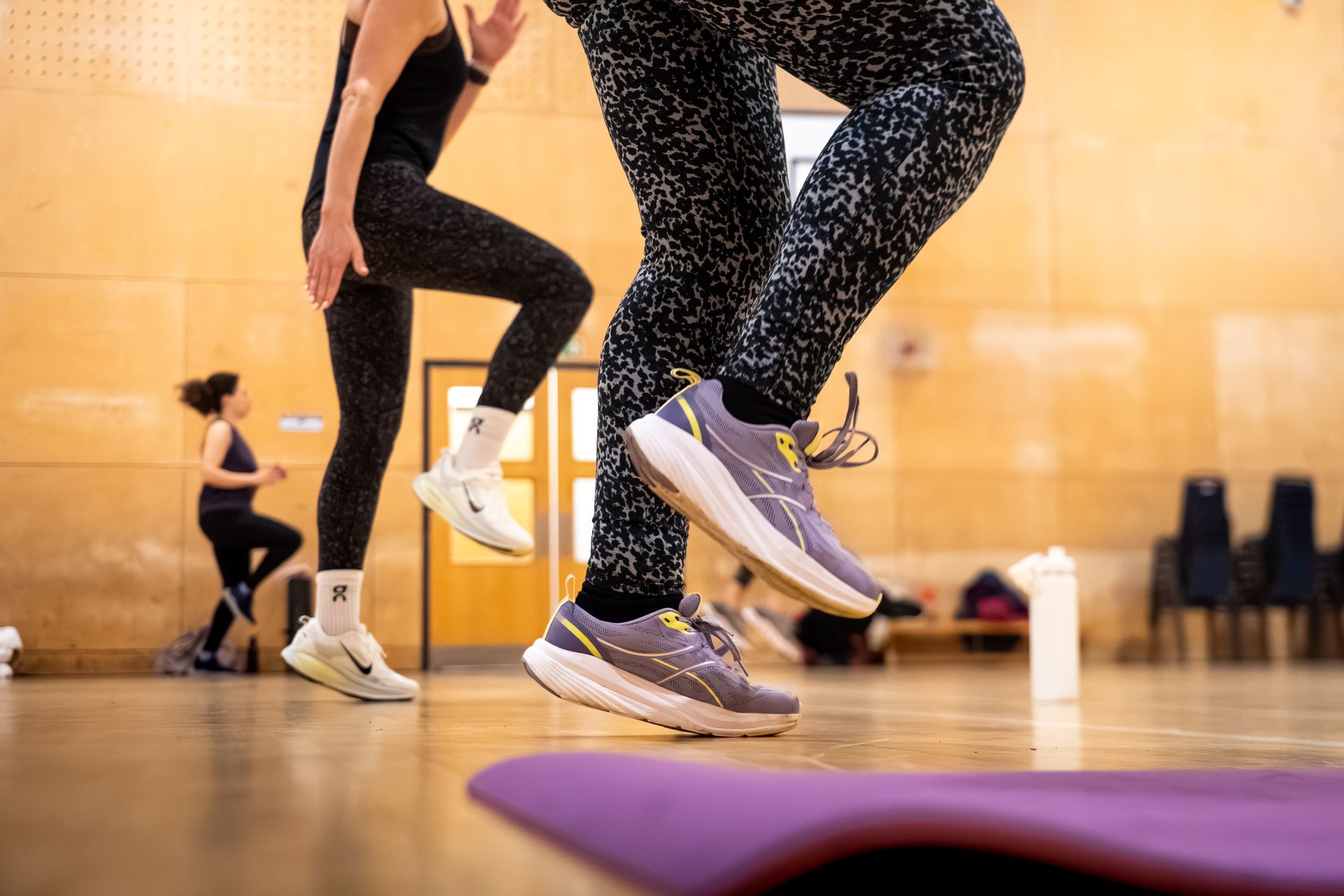 People jumping in a fitness studio, with mats and bright wooden walls in the background