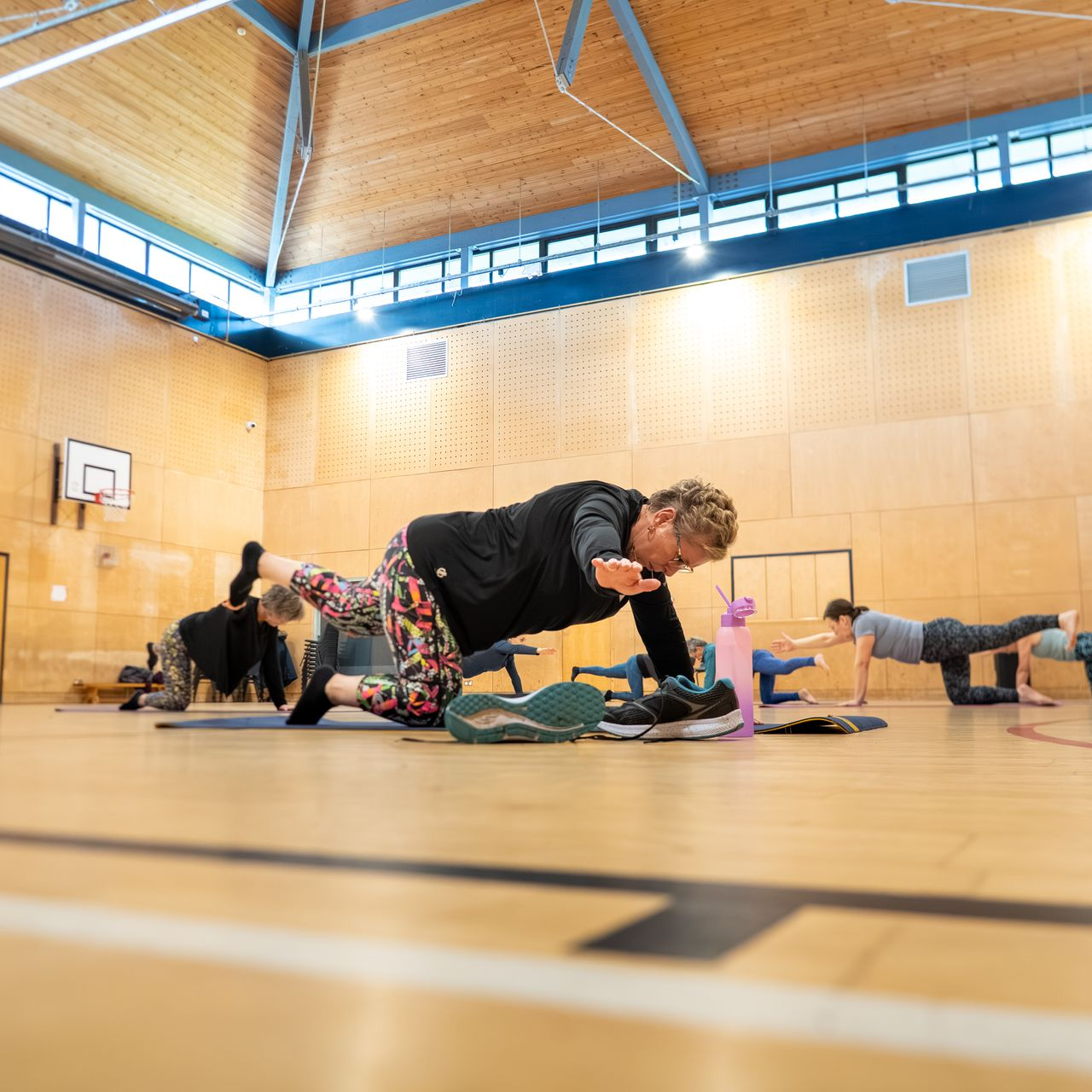 People exercising in a gym, doing plank and balance poses on yoga mats