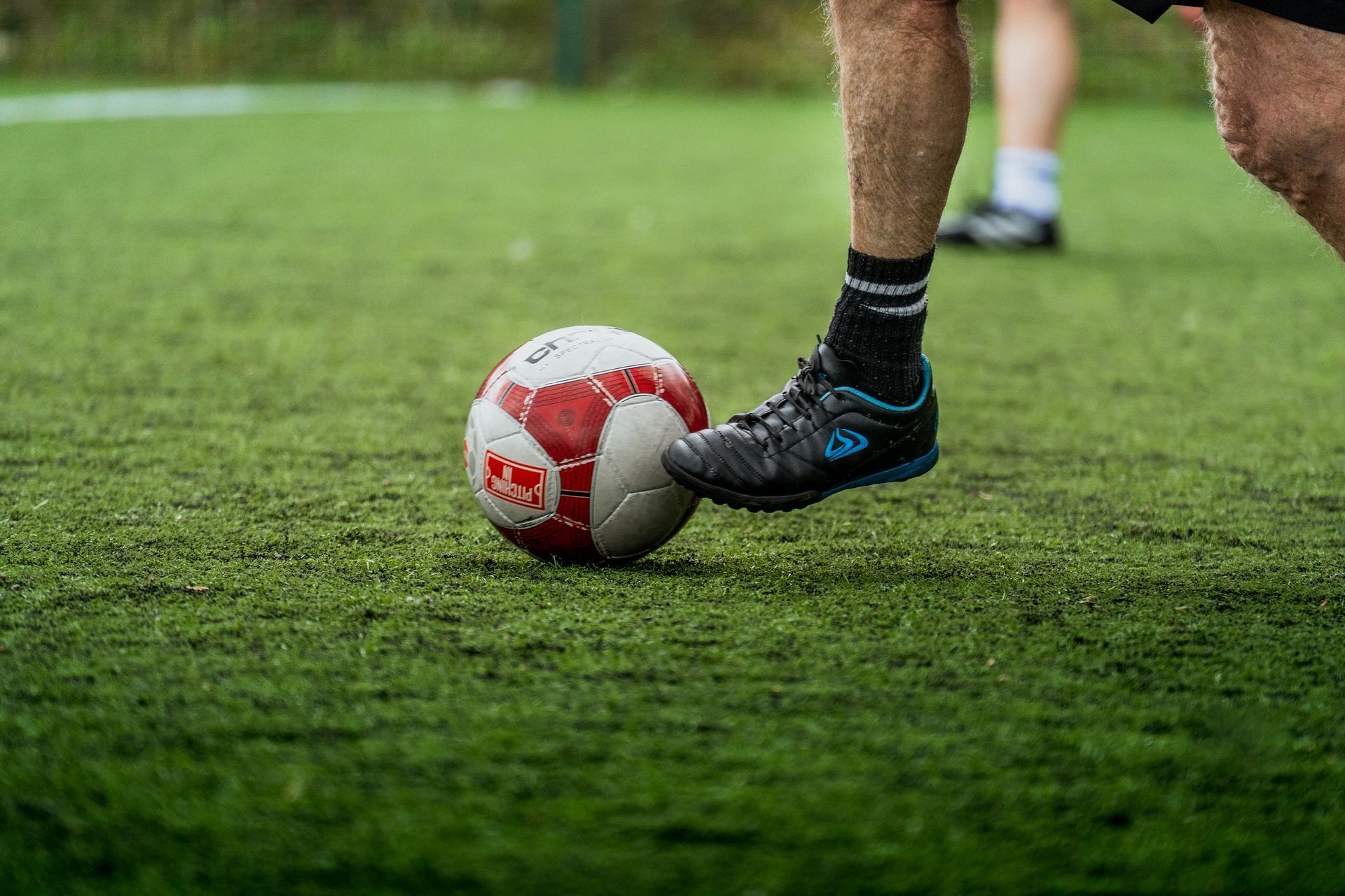 Soccer player’s foot resting on a red-and-white ball on a grassy field