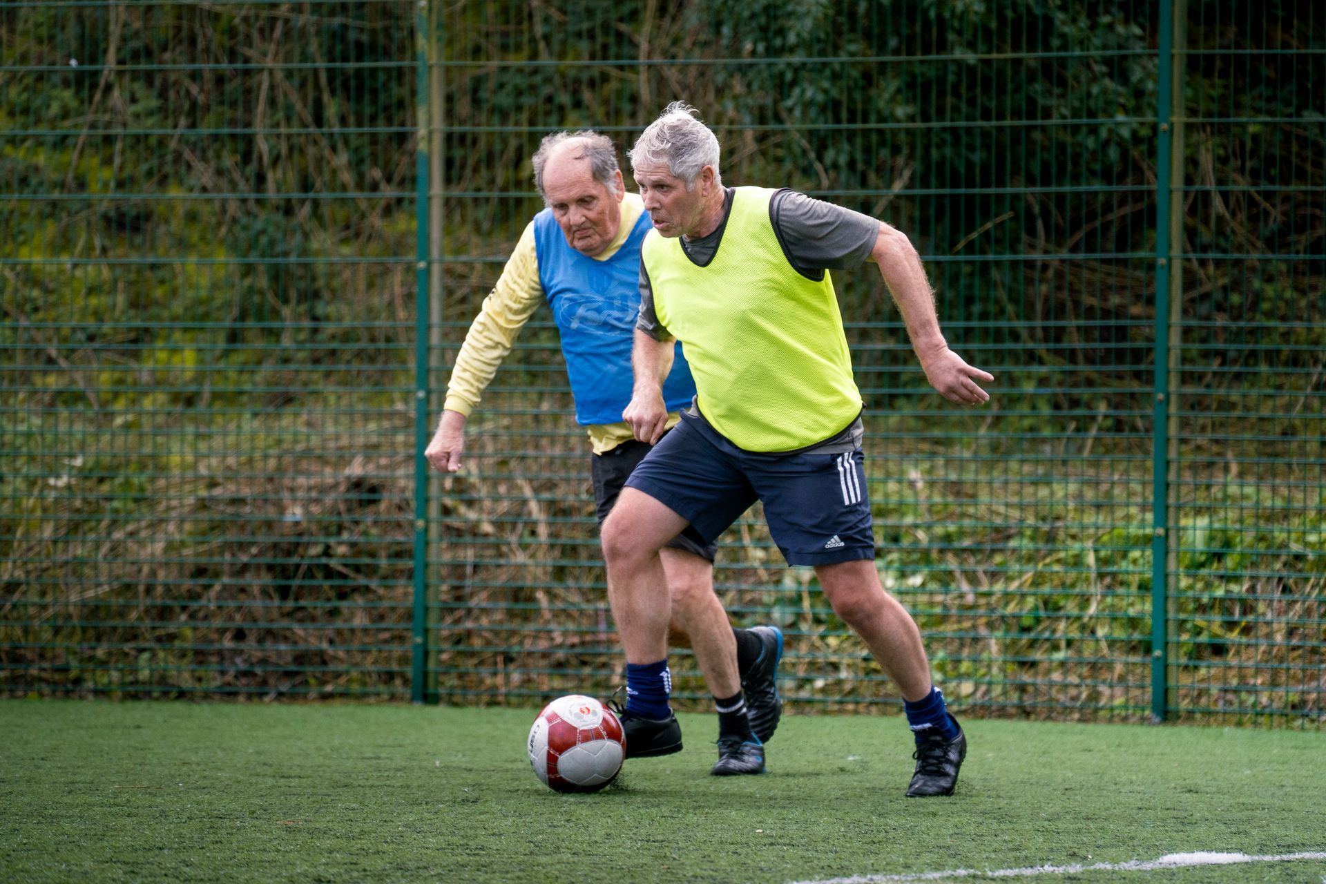 Two players in yellow jerseys chase a soccer ball on an outdoor field.
