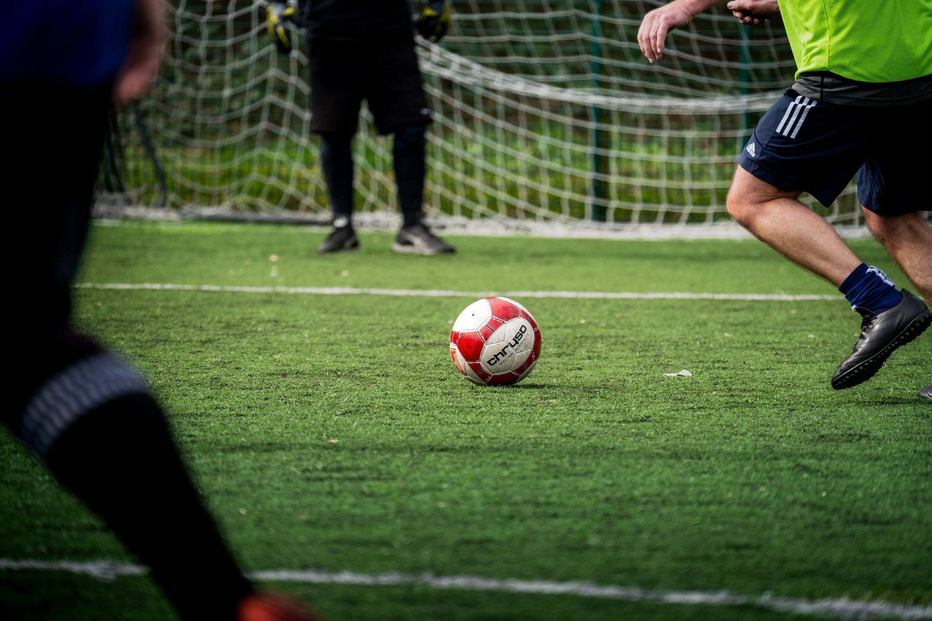 Soccer ball on field near goal as players run toward it