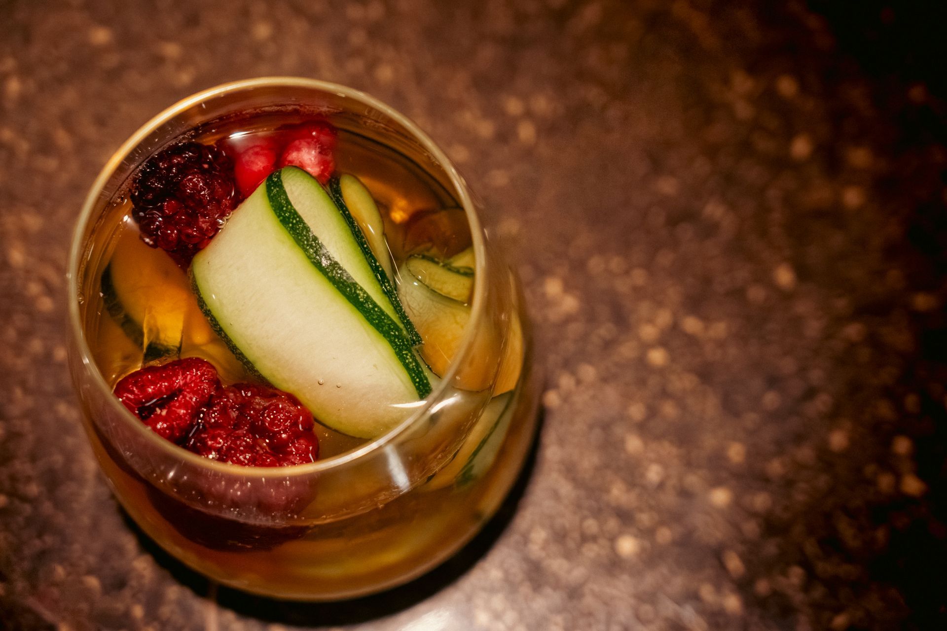 Overhead view of a cocktail with pear slices and raspberries in a glass on a brown surface