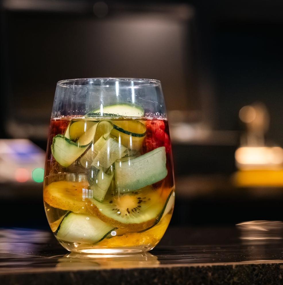 Glass of iced fruit drink with cucumber slices and lemon on a dark bar counter