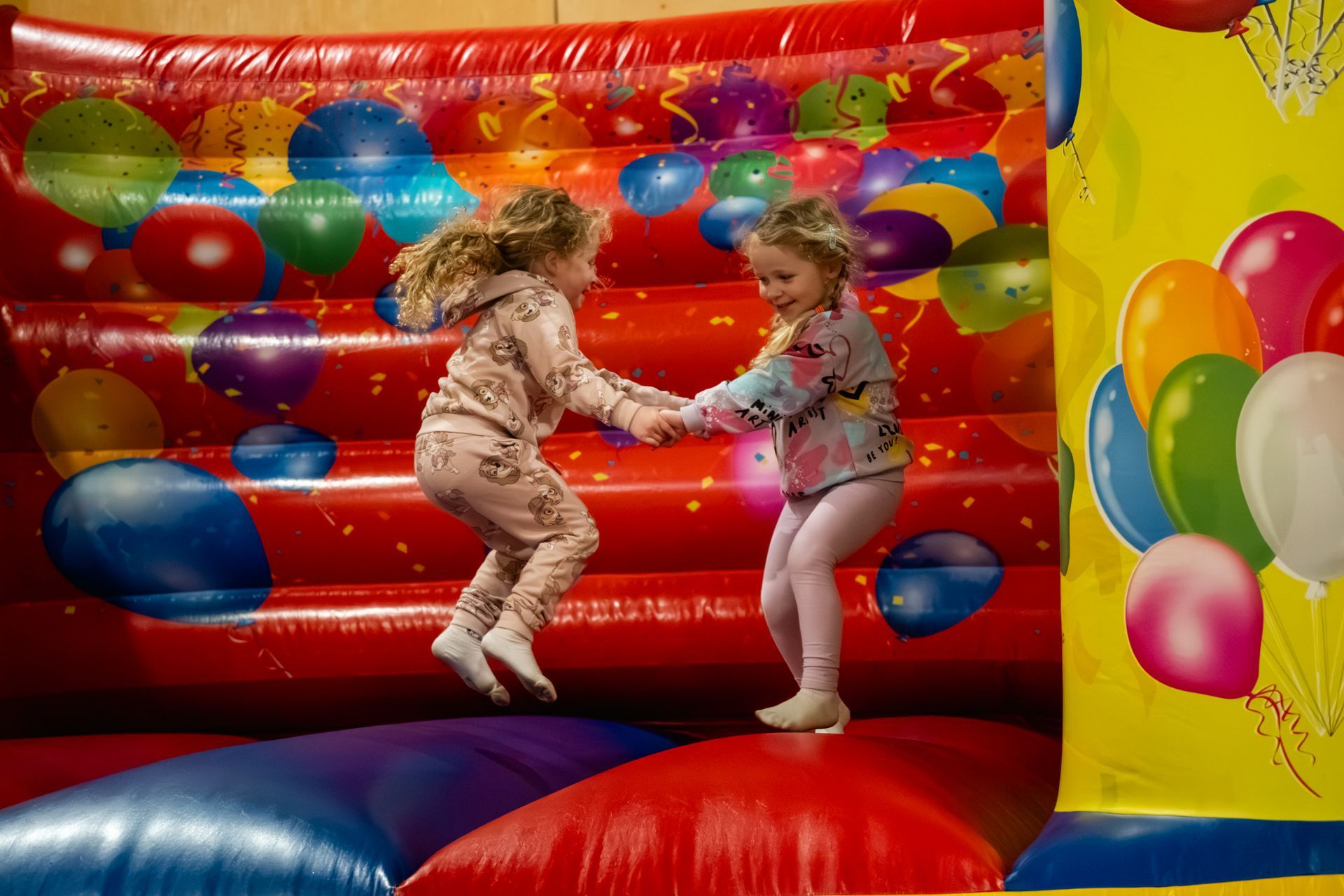 Two children bouncing and holding hands in a colorful inflatable bouncy castle