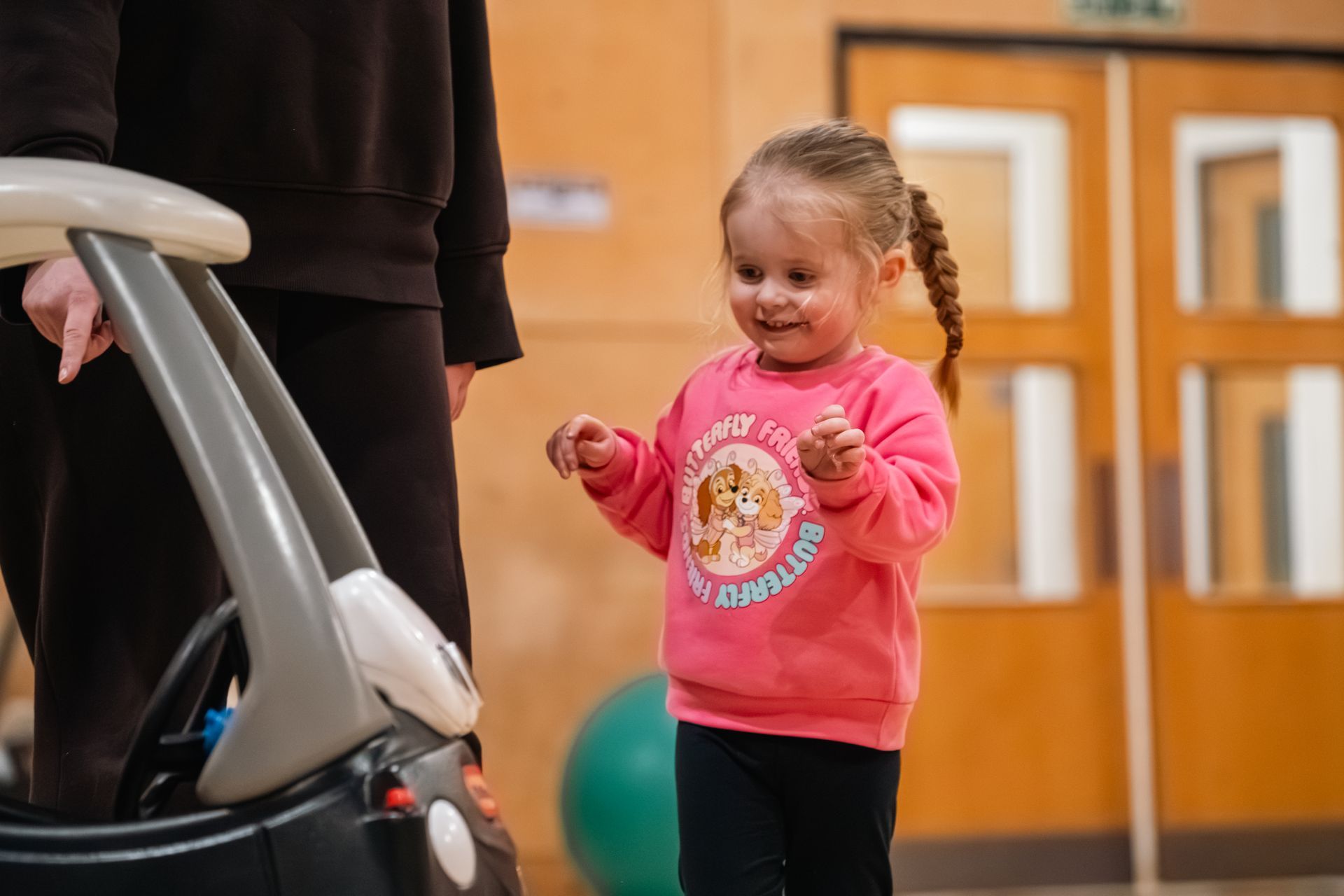 Young child in a pink shirt smiling beside a stroller indoors