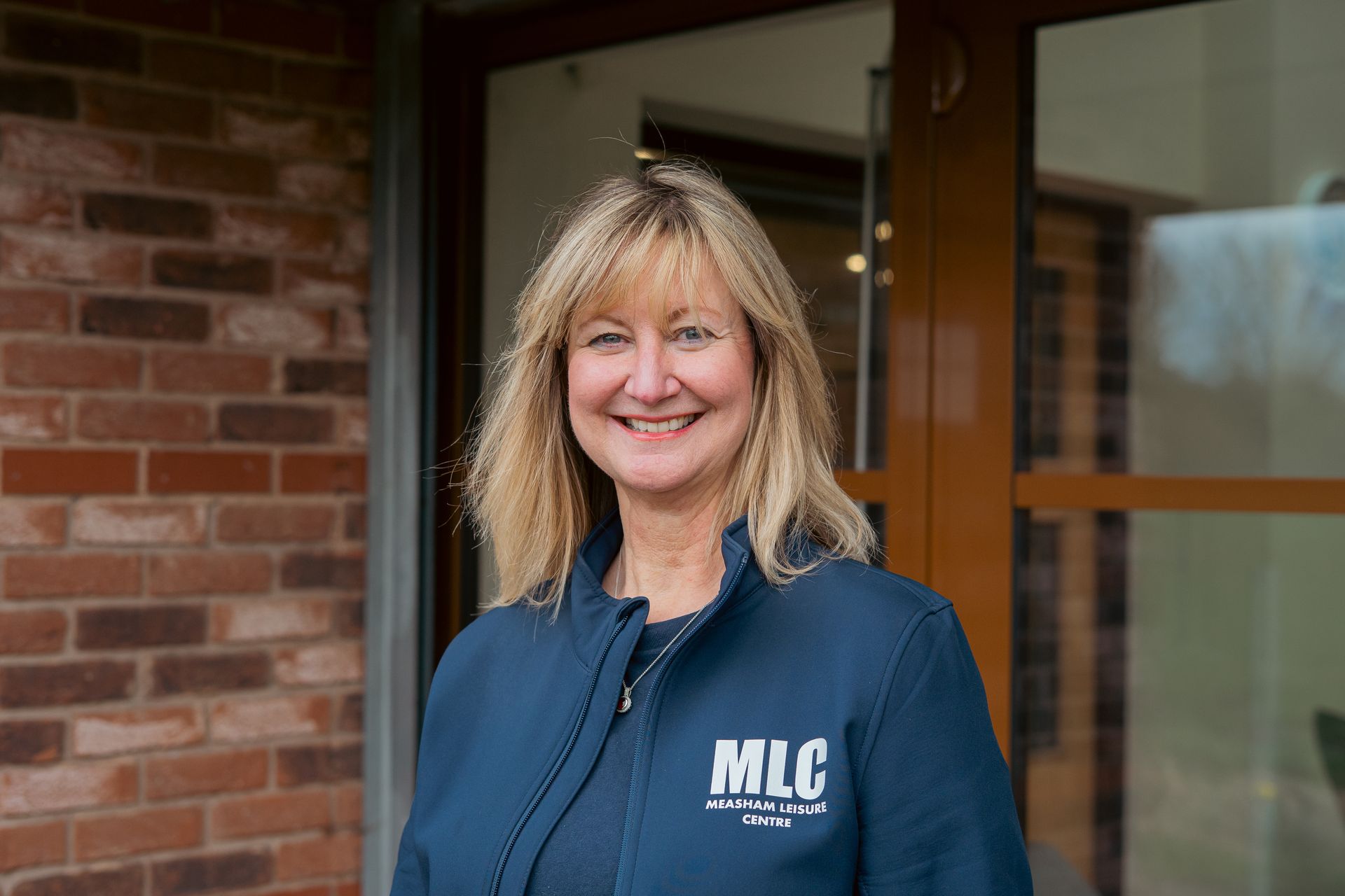 Smiling woman in a navy jacket standing by a brick building entrance
