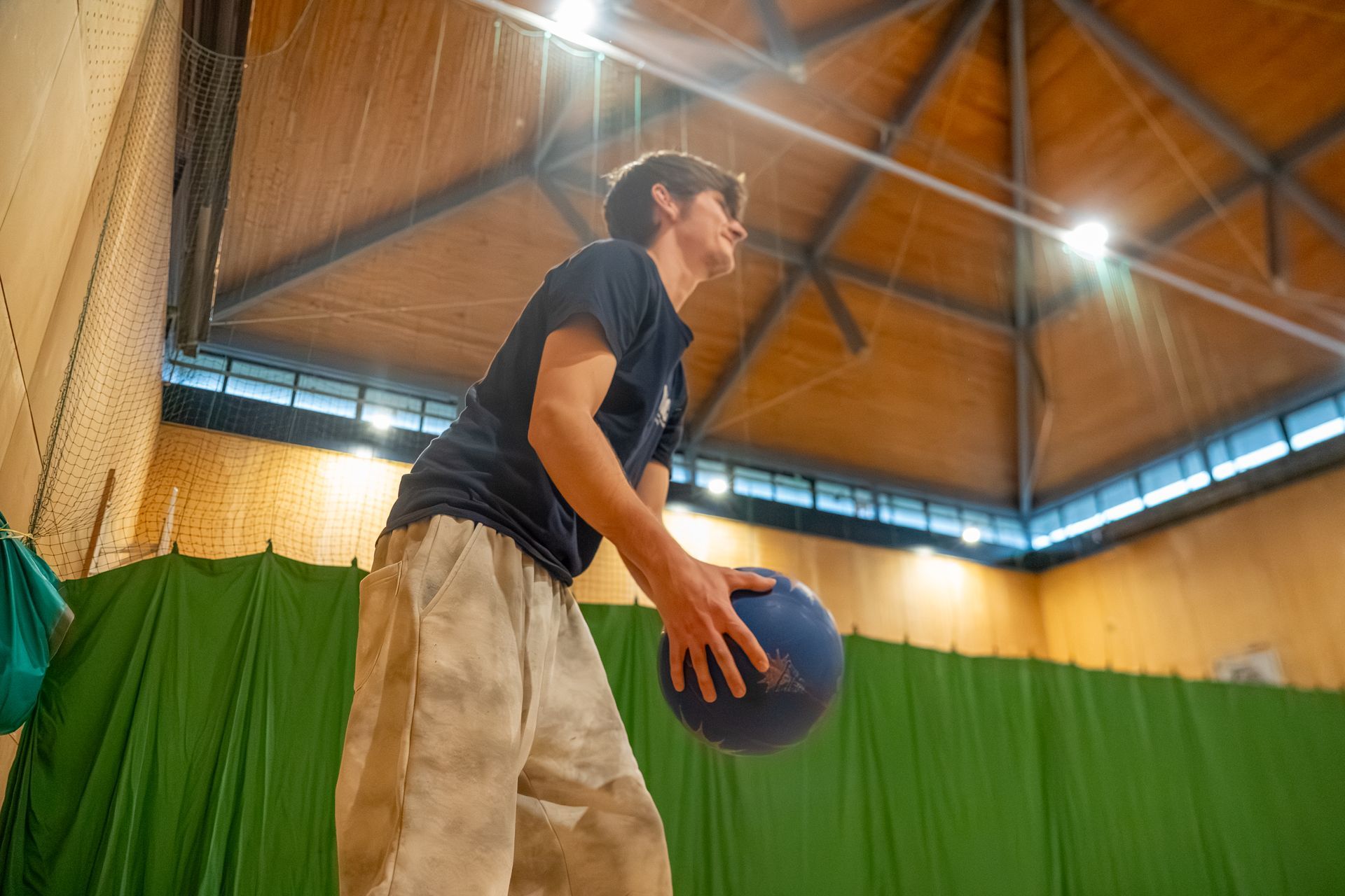 Person holding a basketball indoors on a court with wooden ceiling and green wall padding