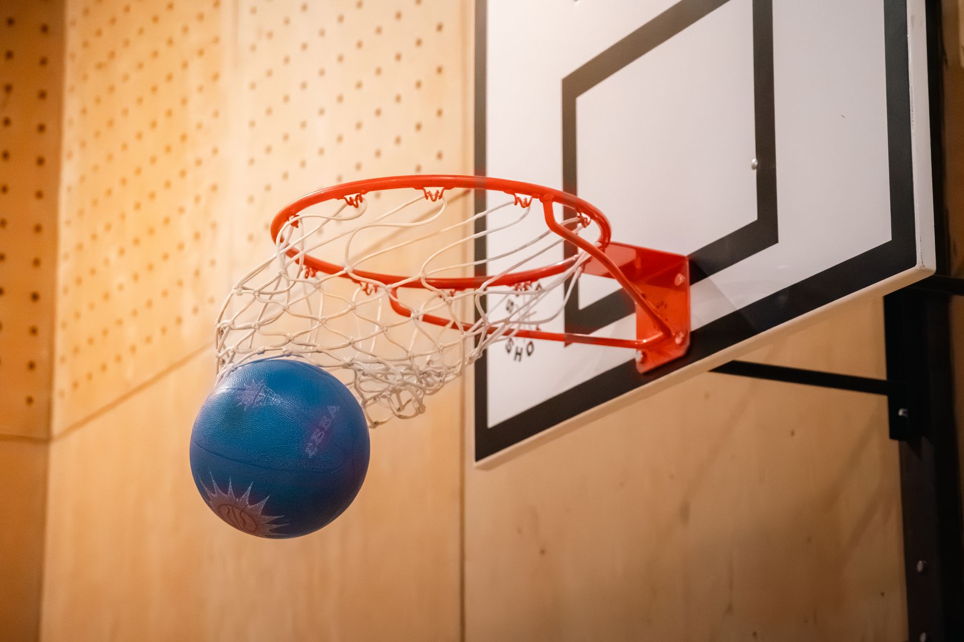 Blue basketball dropping through a red hoop with a white backboard in a gym