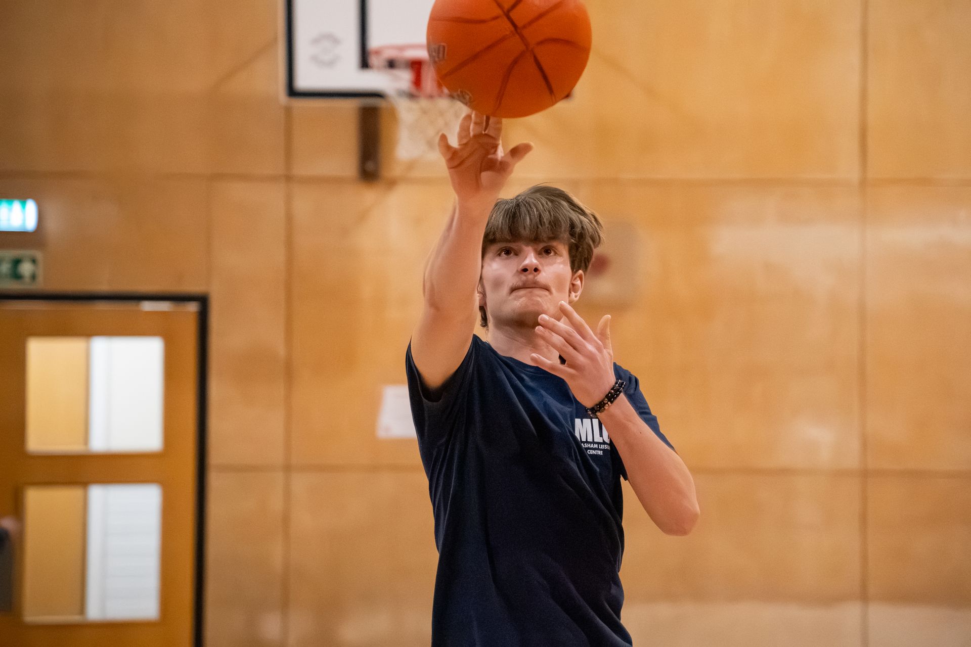 Basketball player reaching up to shoot in a gym, with the hoop in the background.