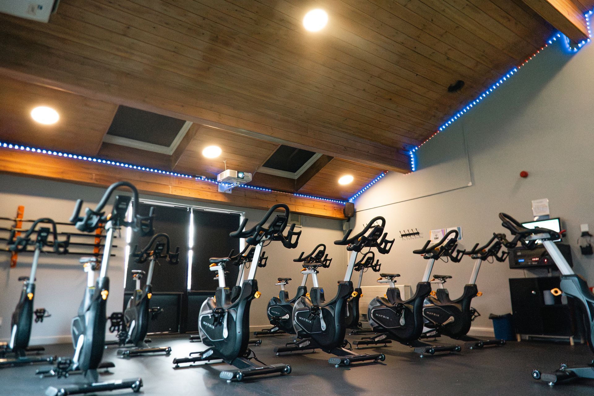 Modern gym with rows of stationary bikes, wood ceiling, and blue accent lighting