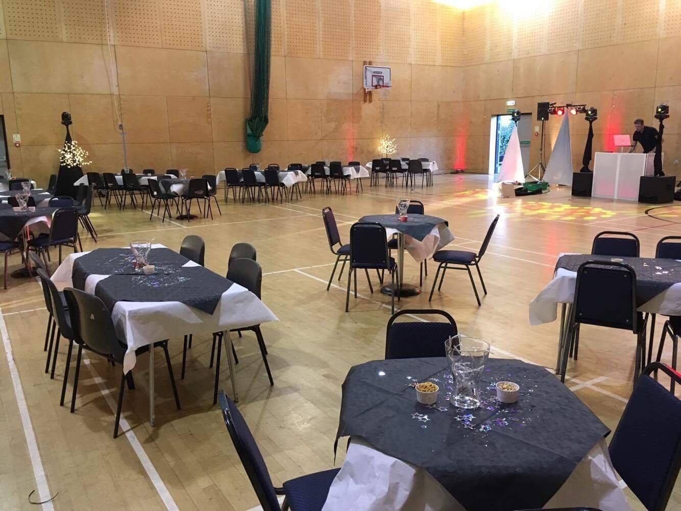 Empty banquet hall with round tables, black chairs, and white tablecloths