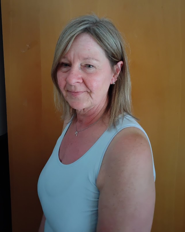 Smiling woman in a light blue sleeveless top against a warm wooden background
