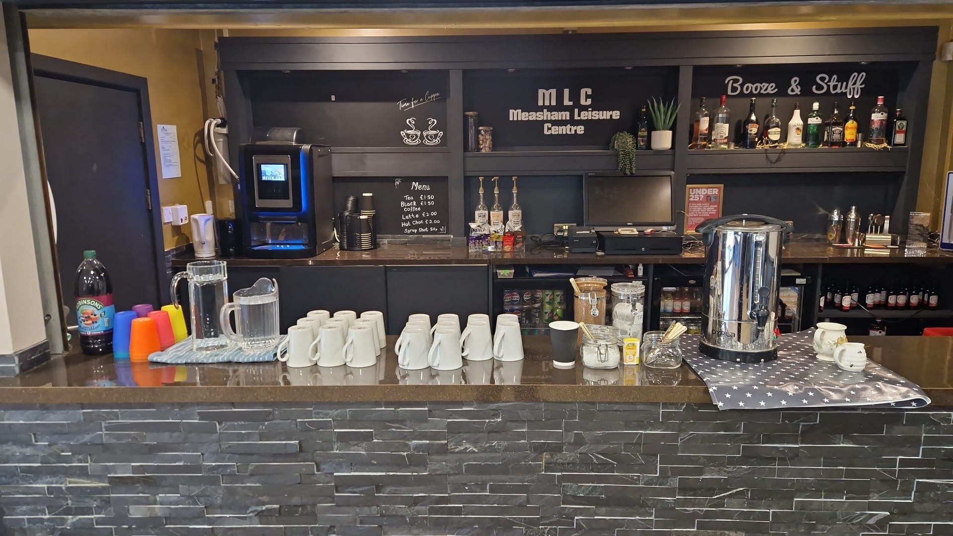 Bar counter with coffee cups, machines, bottles, and shelves in a café or lounge setting