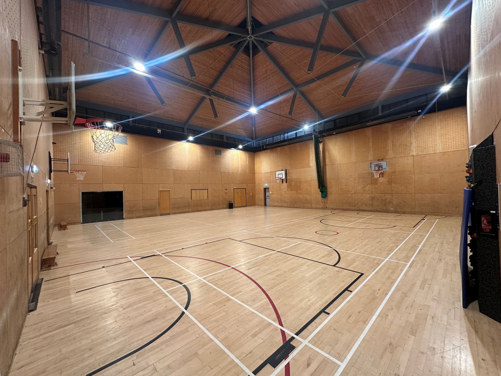 Indoor sports gym with wooden walls, polished court lines, and high arched ceiling lights