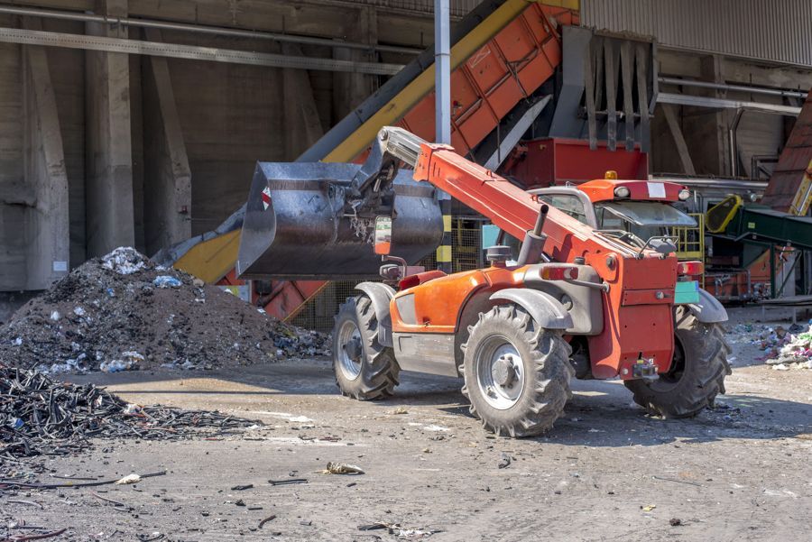 Un tracteur rouge transporte une grosse balle de foin.