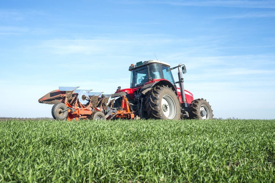 Un tracteur rouge laboure un champ vert.