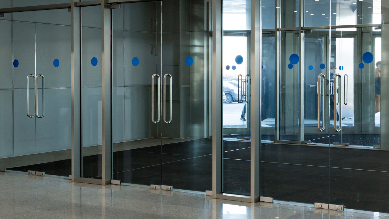 Glass office entrance with double doors, blue circular decals, and reflections on the polished floor