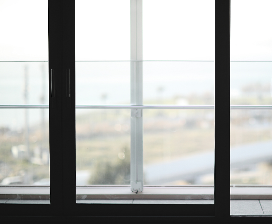Blurred view through large black-framed windows with a bright outdoor landscape beyond.