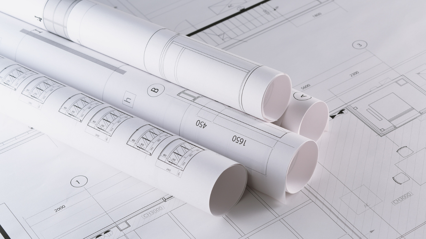 Rolled architectural blueprints on a desk with faint floor plan drawings underneath
