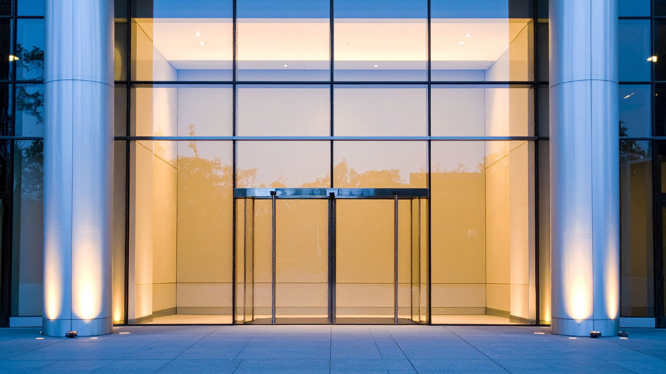 Modern glass building entrance with warm interior lighting and blue-lit columns