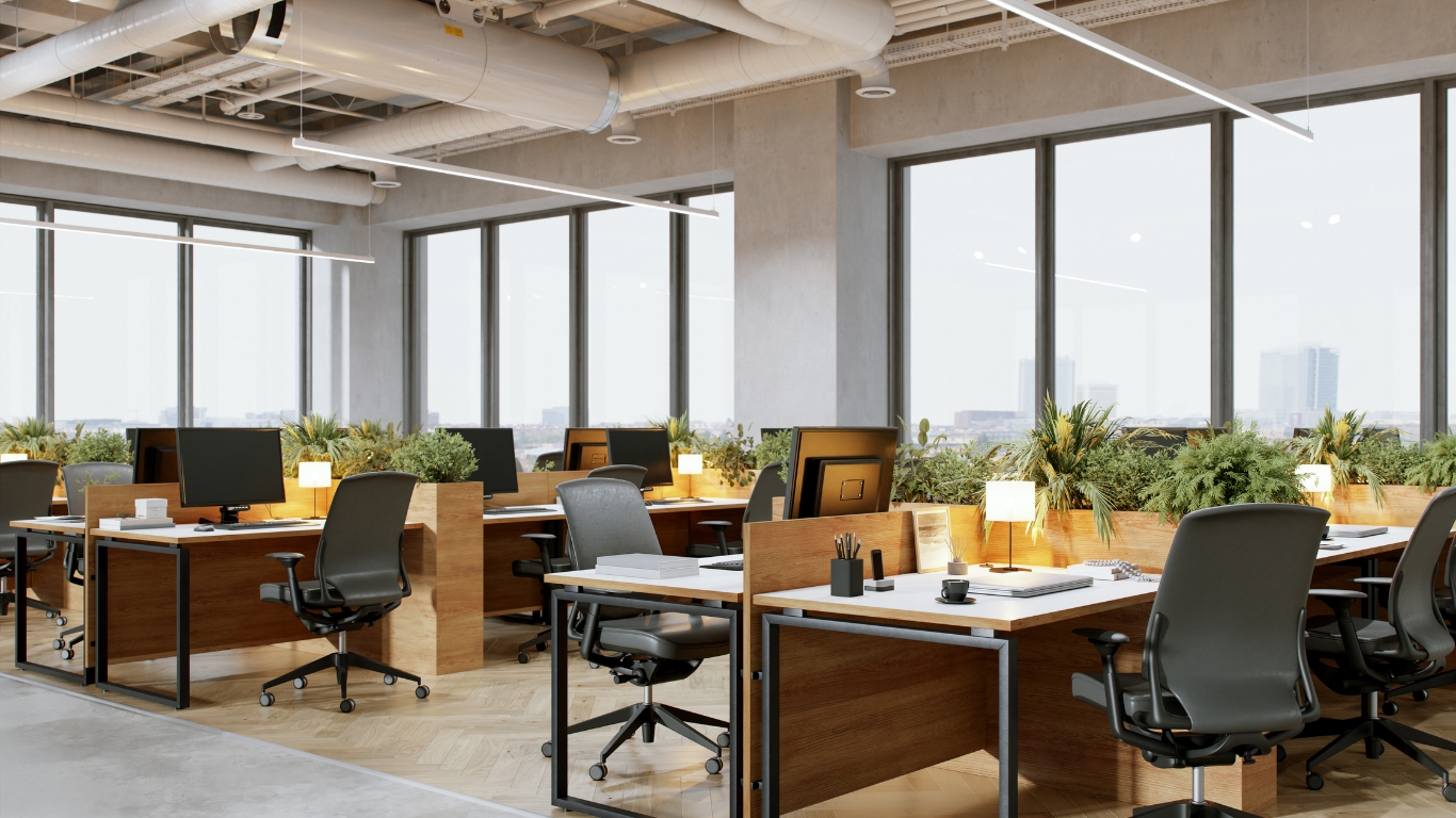 Bright open-plan office with wooden desks, black chairs, computers, and large windows.