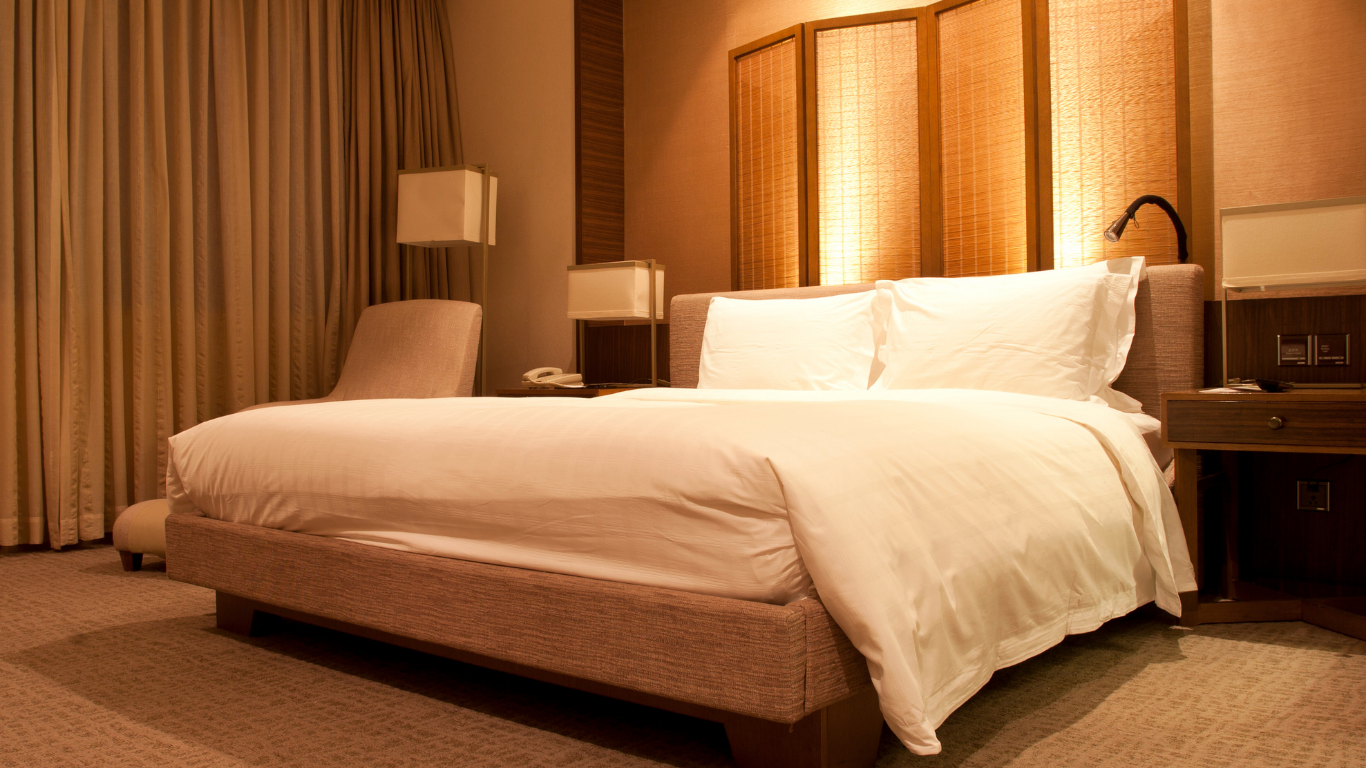 Warmly lit hotel room with a large white bed, bedside lamps, and floor-to-ceiling curtains.