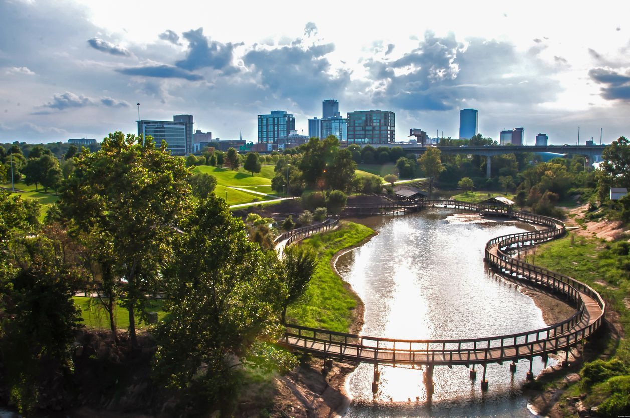 Curving riverwalk through a green park with a city skyline in the background