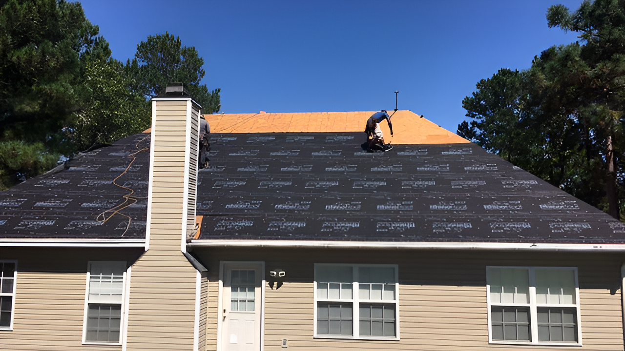House roof under repair with new shingles on the right side and an exposed chimney against a blue sky