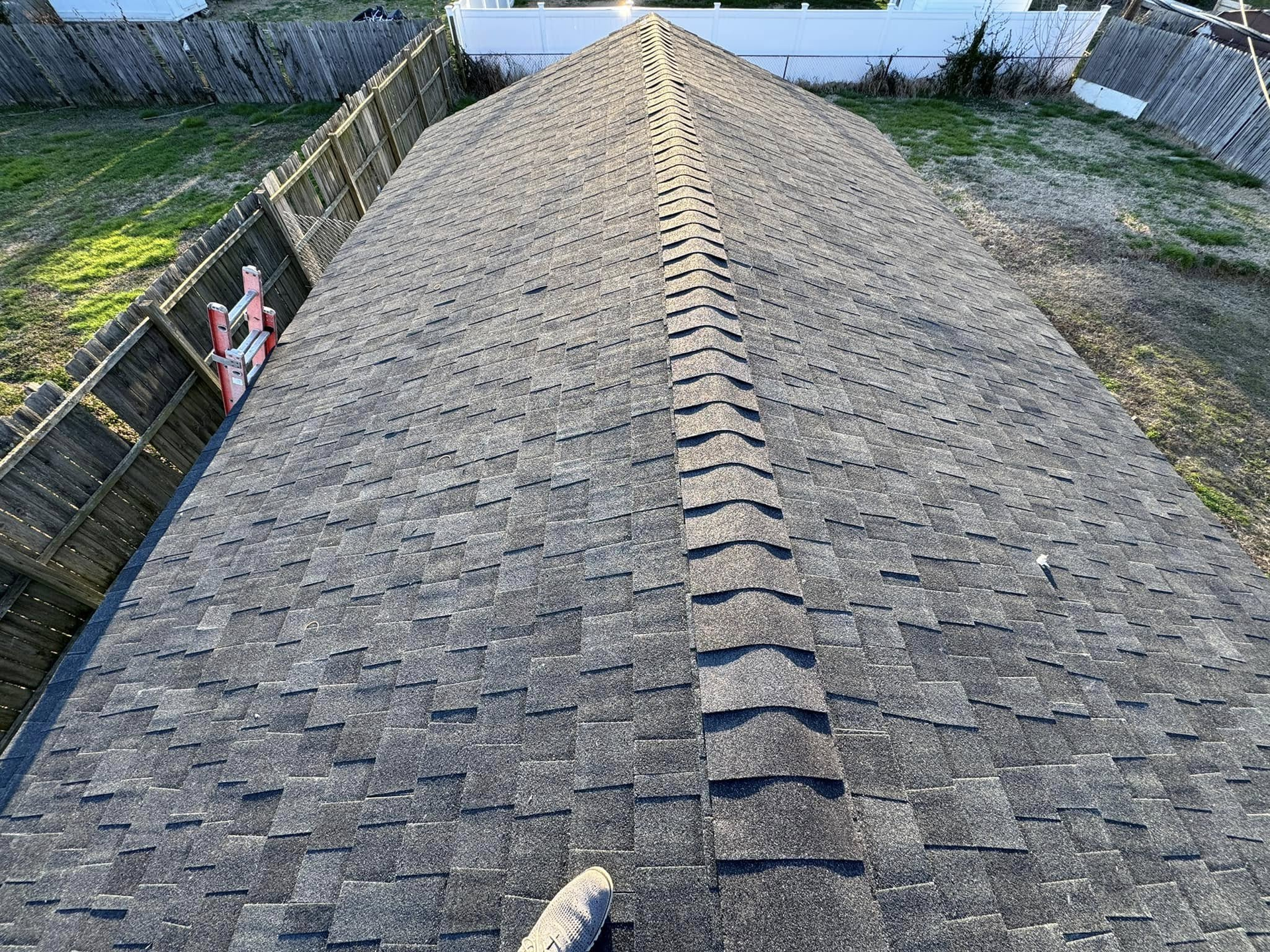 Aerial view of a shingled roof with a ridge vent and fenced yards on both sides.