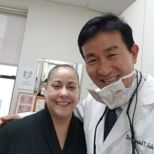 Two smiling people posing together in a clinic, one in a white coat and one in black scrubs