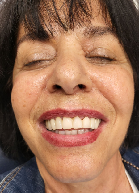 Close-up of a smiling woman with eyes closed, showing red lipstick and white teeth.