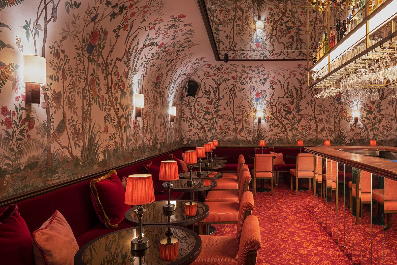 Cozy bar interior with floral wallpaper, red seating, small tables, and dim lamps.