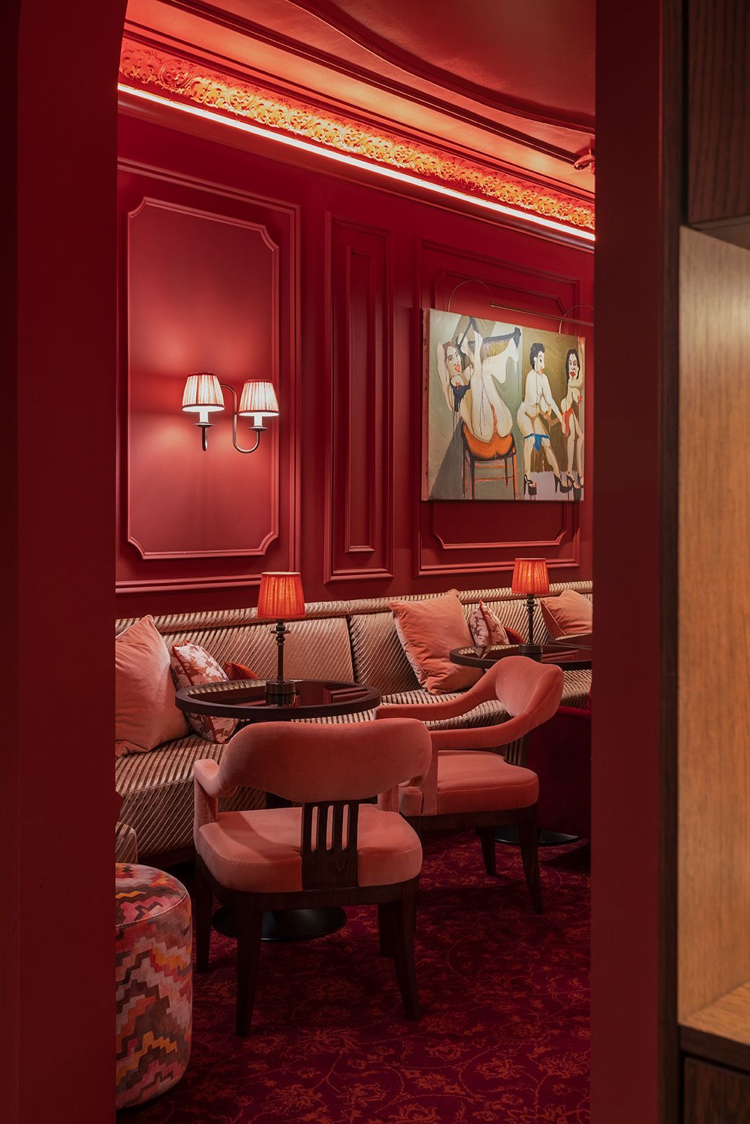 Red-walled lounge with a built-in sofa, chairs, artwork, and lamps, viewed through a doorway.