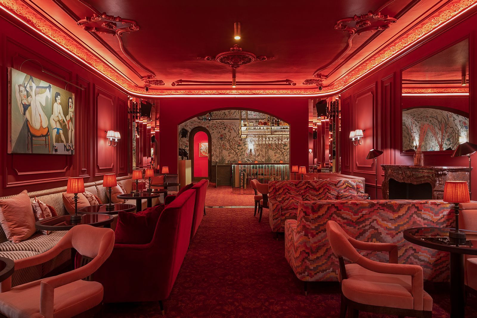 Red, ornate bar interior with plush seating, dim lighting, and a glimpse of a bar in the background.