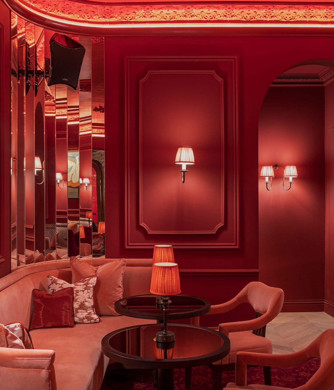 Red-themed lounge area with velvet seating, round tables, and wall sconces.