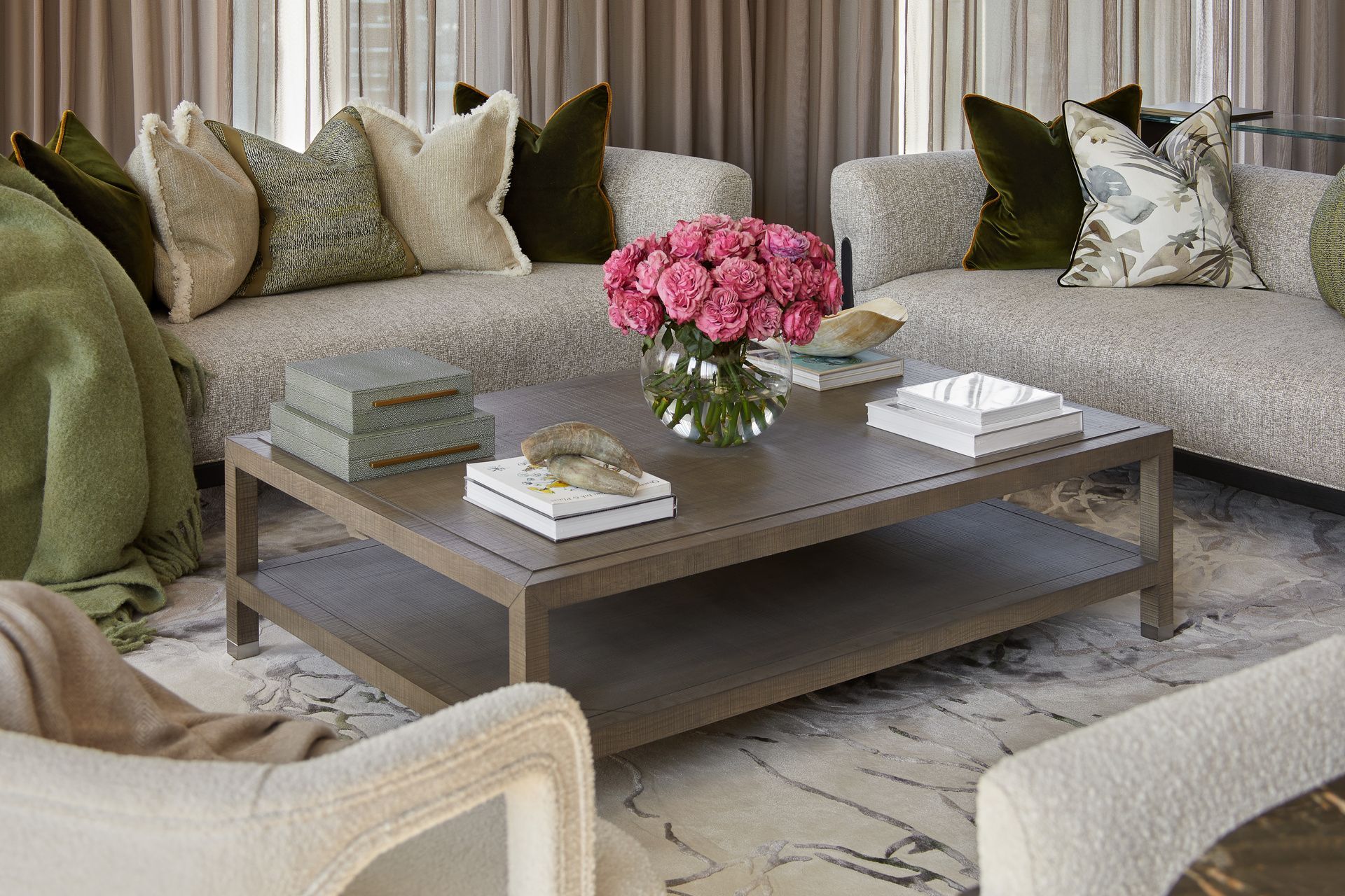 Cozy living room with a gray sectional sofa, coffee table, and pink flowers. Green pillows and throw.
