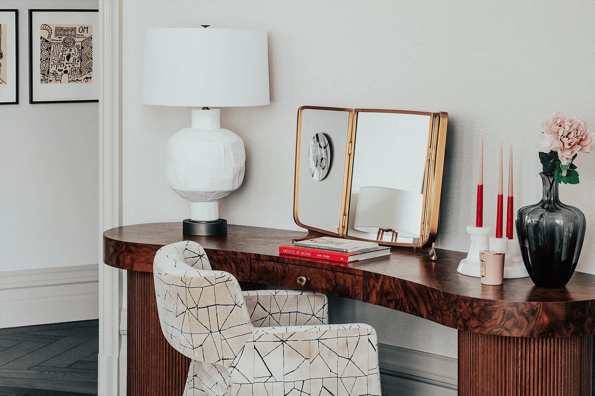 Vanity table with chair, lamp, mirror, and decor. Light-colored walls and art.