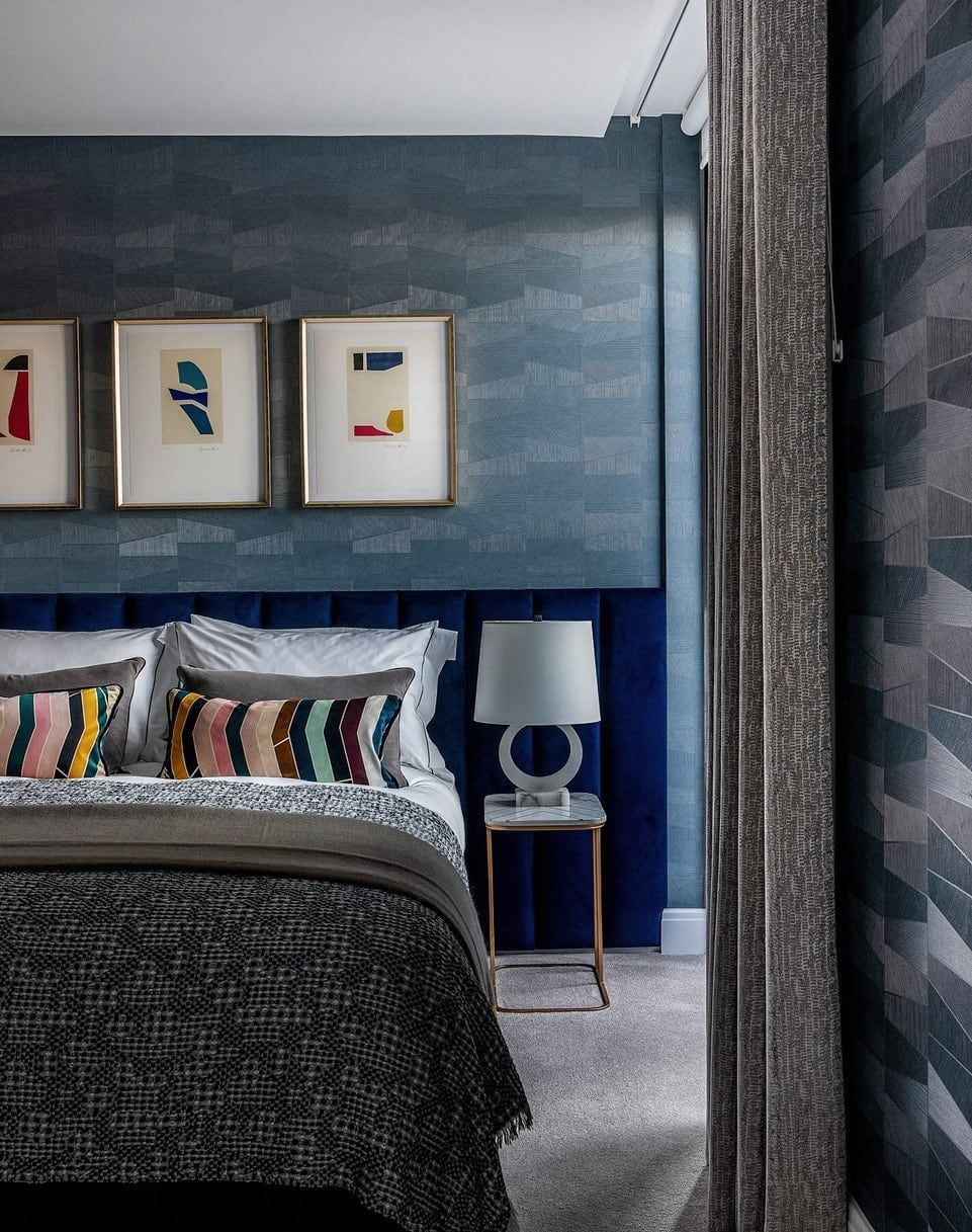 Bedroom with blue textured wall, bed, artwork, side table, and curtain.