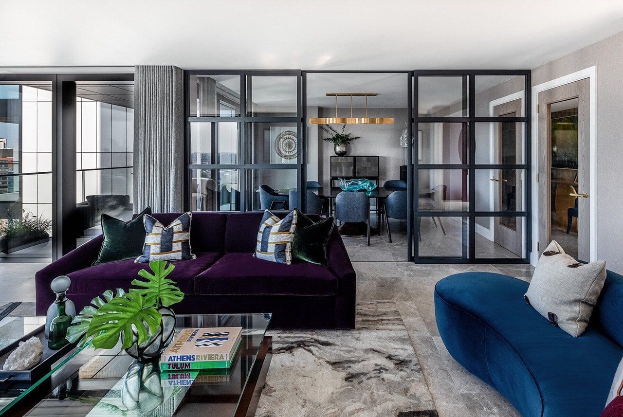 A luxurious living room with a city view. A white armchair sits by a large window, a purple couch is in the foreground.