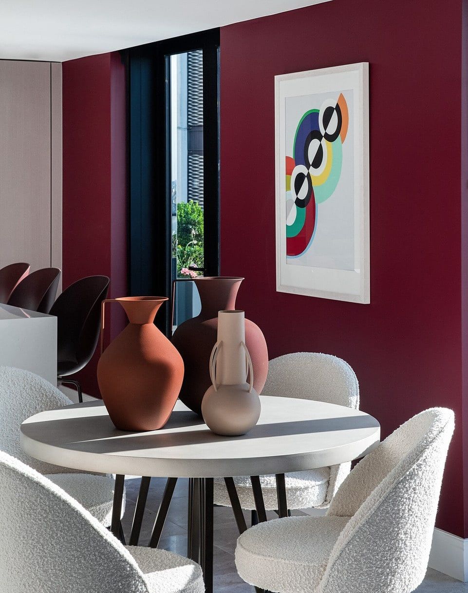 Dining room with a burgundy wall, round table, art, and vases.