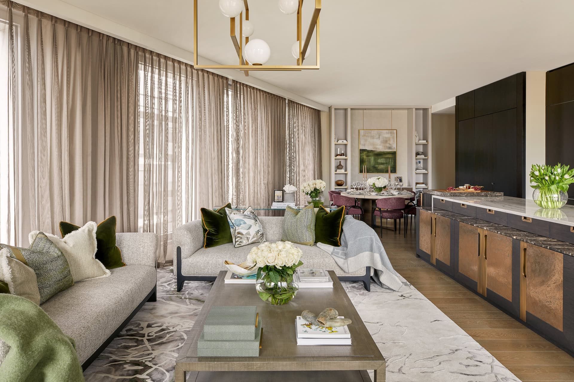 Luxurious living room with light gray sofa, gold chandelier, and open dining area.