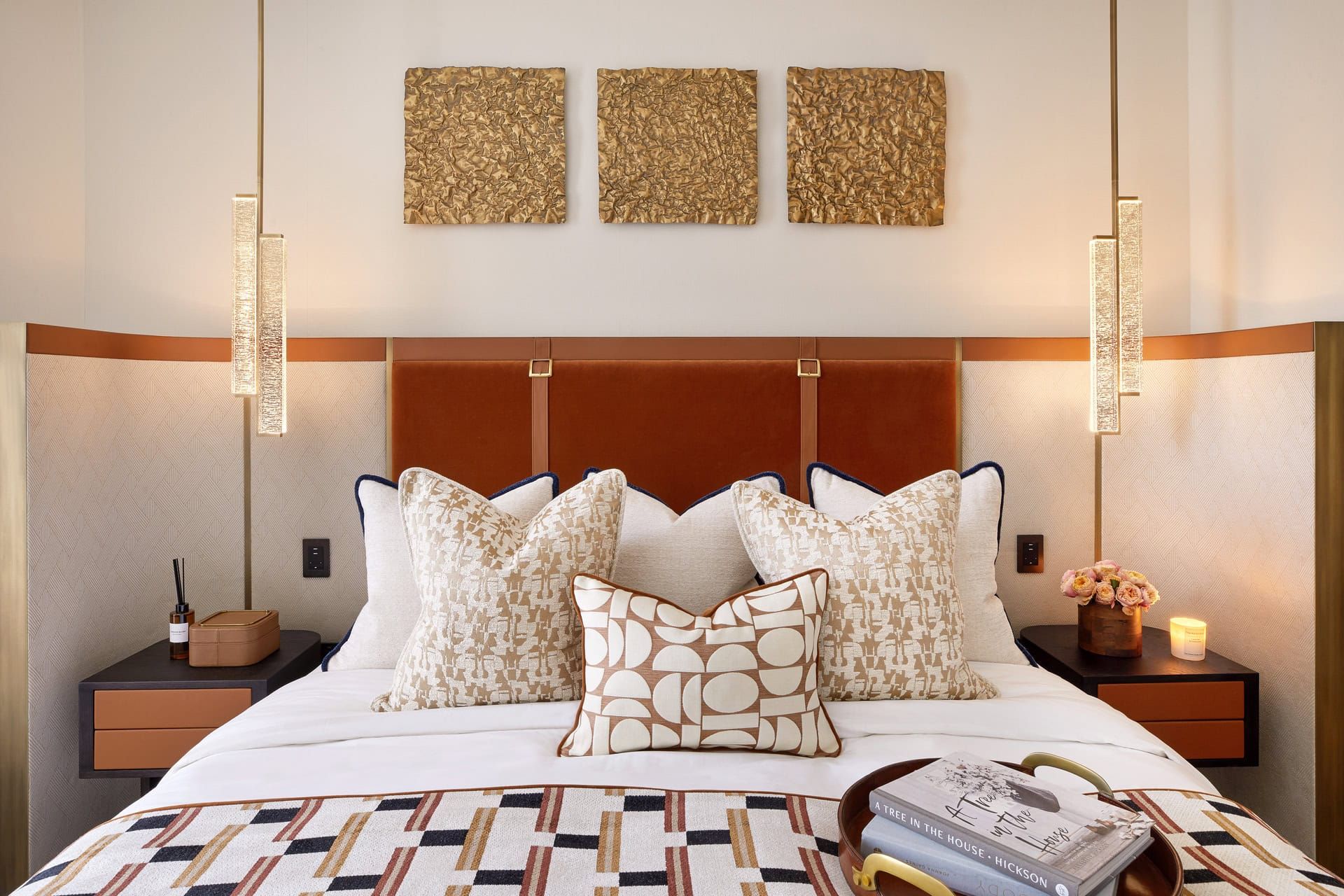 Cozy bedroom with a bed, decorative pillows, artwork, bedside tables, and hanging lights.