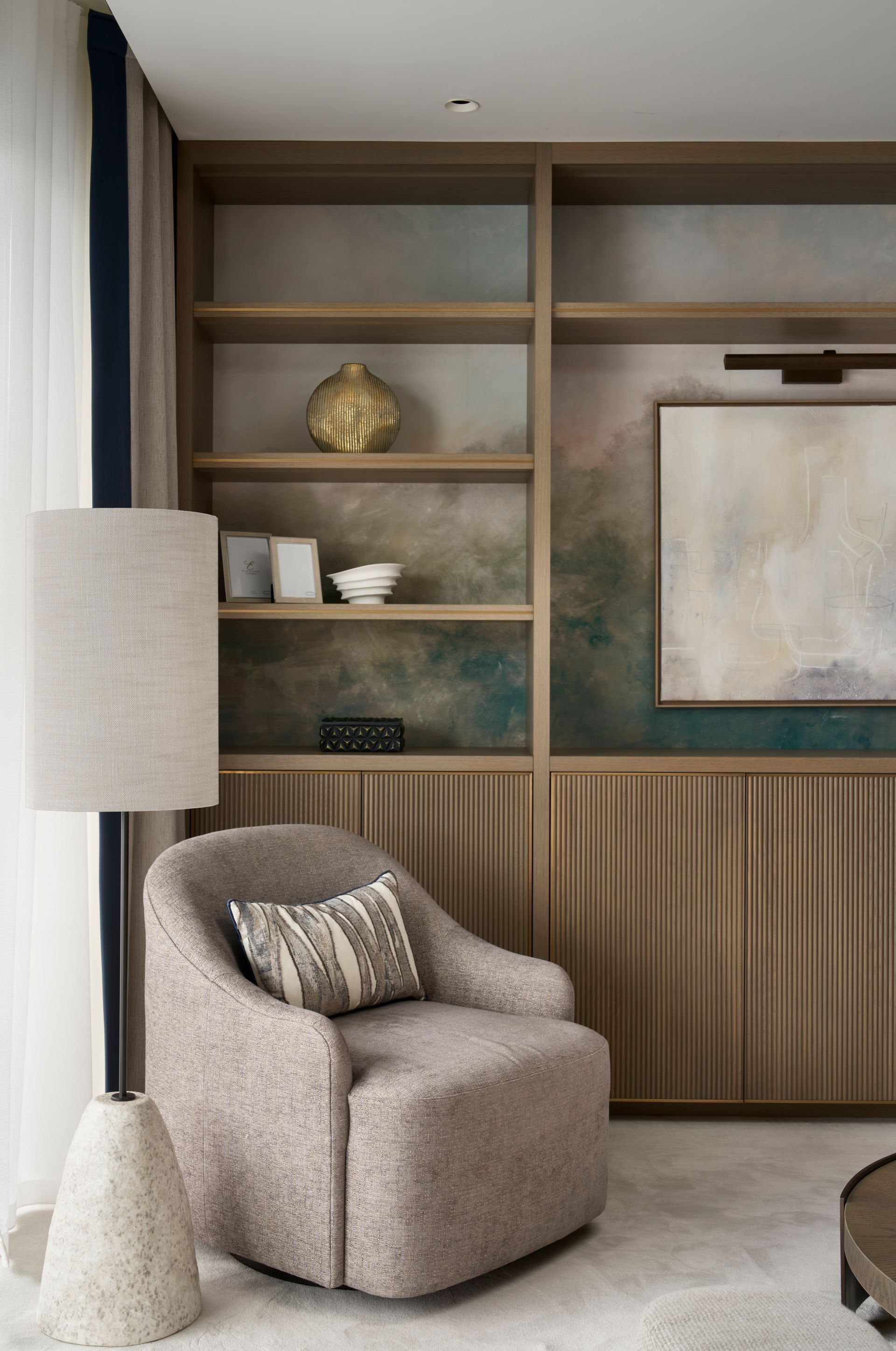 Cozy reading nook: beige armchair, textured floor lamp, wooden bookshelf with decor, and artwork, in a room.