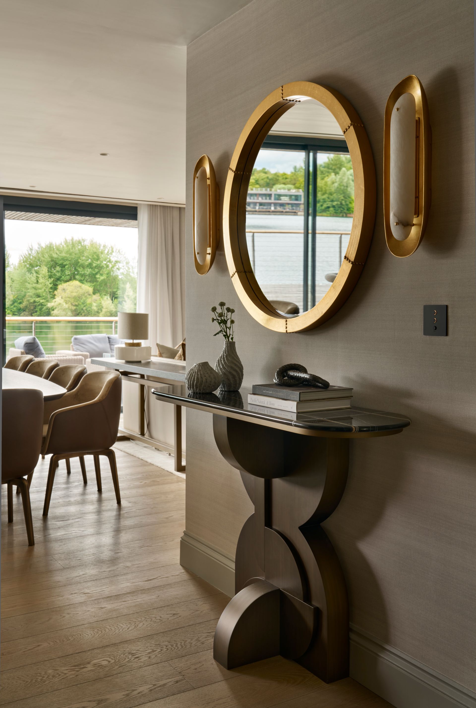 Hallway with oval gold mirror, console table, and sconces; adjacent dining area visible.