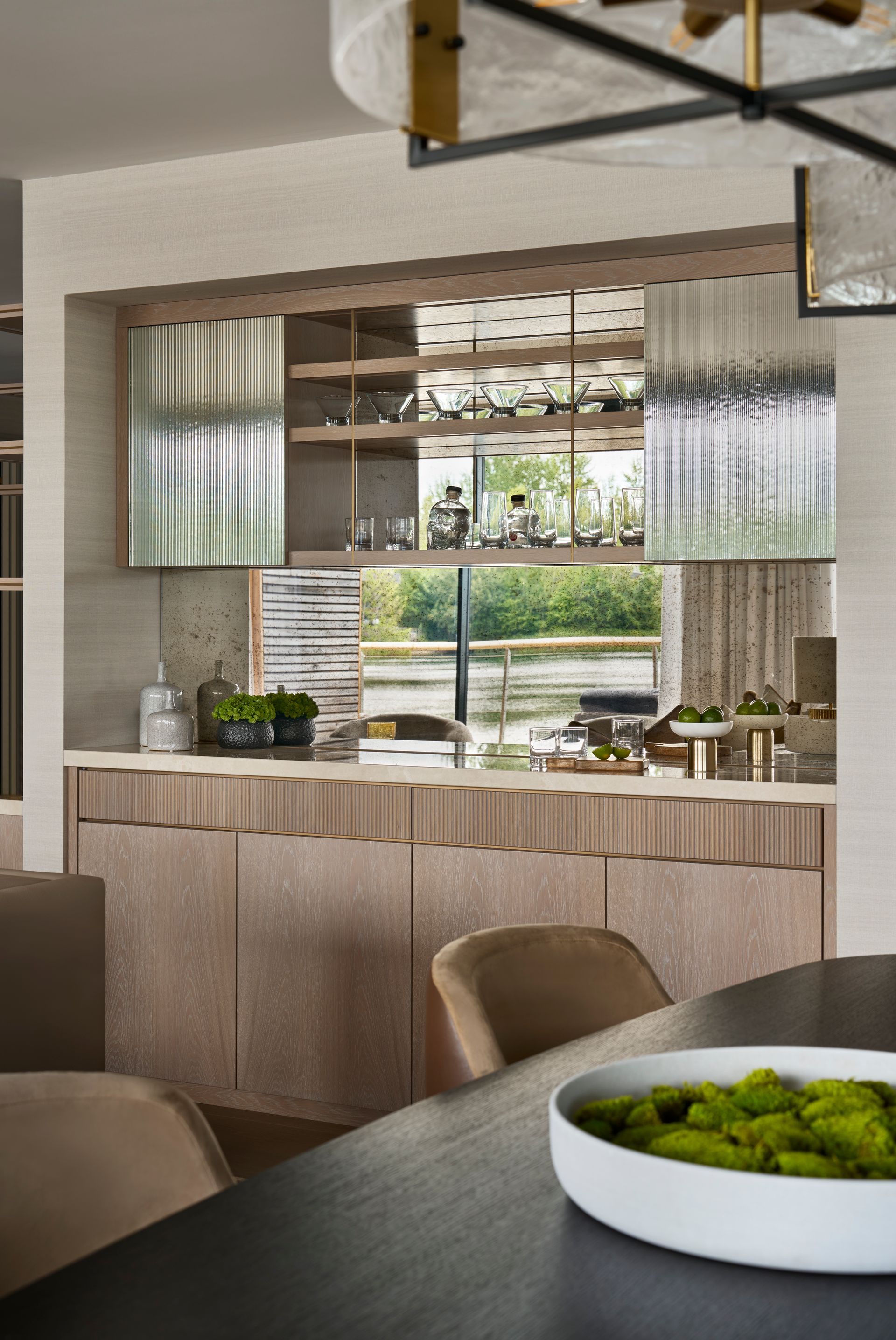 Bar area with wood cabinets, textured glass, and a mirror. A round table in the foreground has a white bowl of moss.