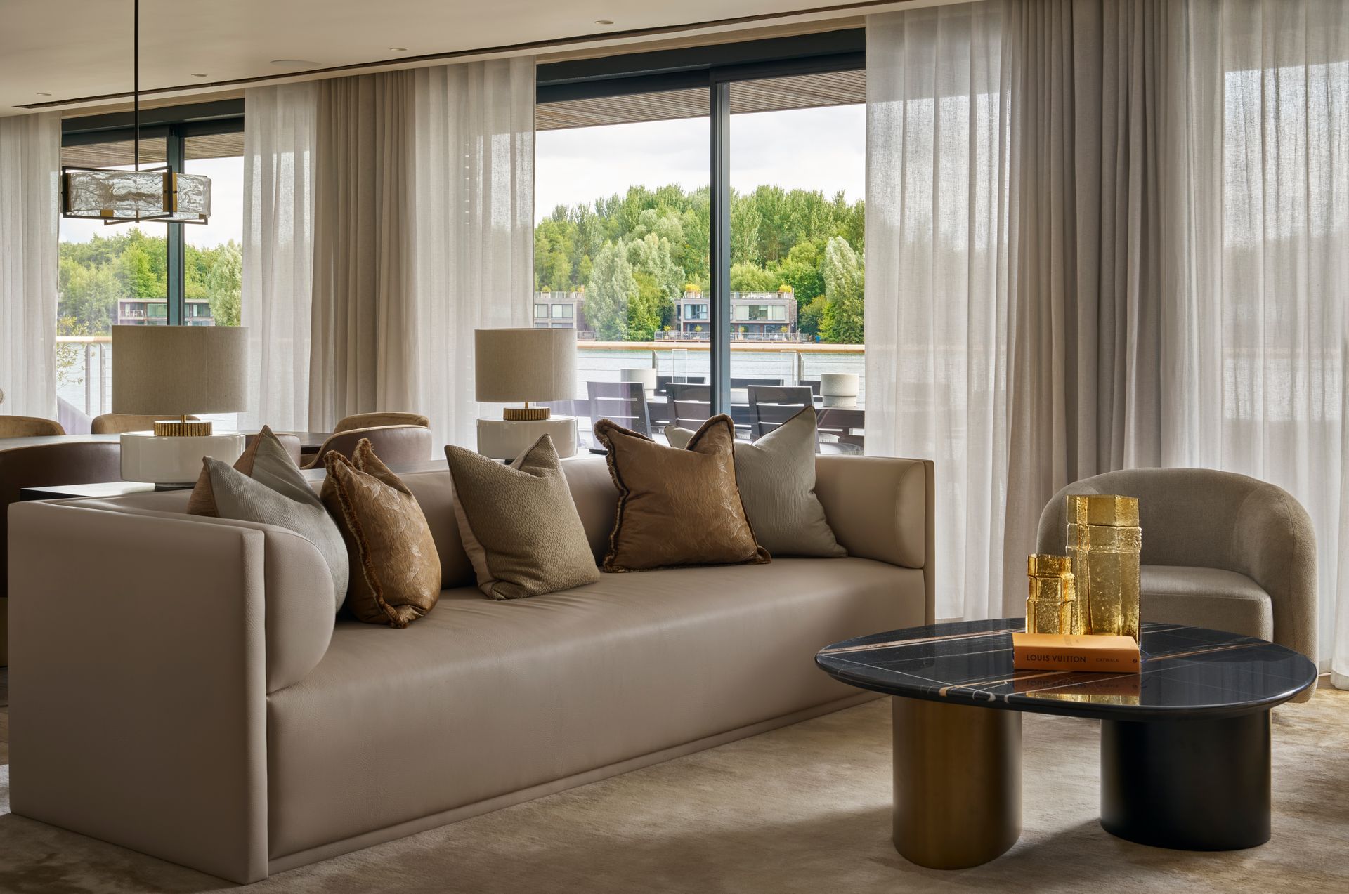 Living room with a beige couch, pillows, and a round black coffee table with a scenic view.